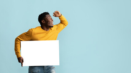 Black guy with blank advertising board looking at copy space