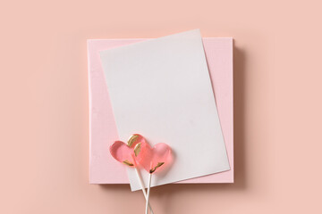 Valentine's day greeting card with empty blank and two pink lollipops sweets on pink background. View from above. Space for text. Minimal flat lay.