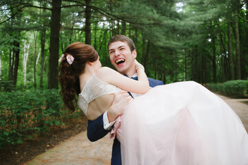 Fototapeta premium The groom holds the bride in his hands and laughs out loud in the park