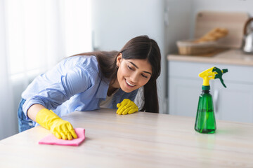 Cheerful young woman cleaning dining table at kitchen
