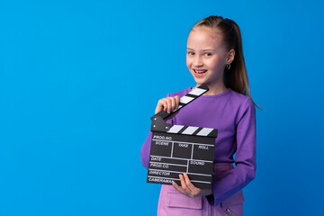 Smiling girl holding clapper board against blue background