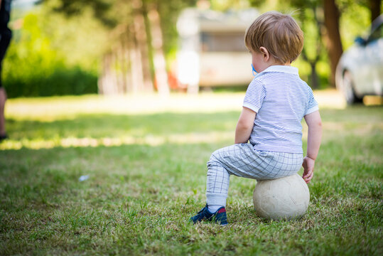Photo from behind of a sweet little boy sitting on the ball on a sunny day