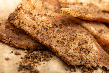 thinly sliced homemade lard with pepper on white oiled paper, close-up, selective focus.