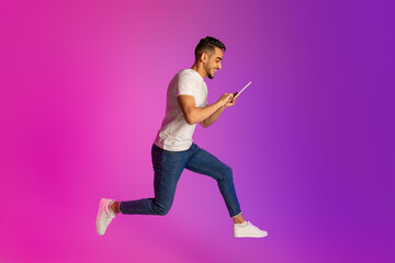Full length of young Arab guy with tablet computer jumping in neon light, free space. Cool app or...