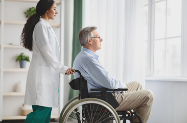 Young female doctor helping senior man in wheelchair indoors, copy space