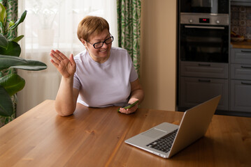 An elderly woman works at a laptop and communicates via video call. Modern technologies and aged people concept