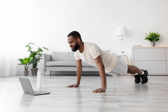 Attractive serious young african american man with beard in white sportswear in minimalist living room