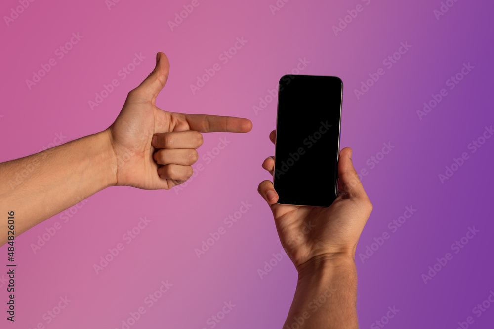 Poster Unrecognizable young guy pointing at smartphone with empty screen in neon light. Mockup for ad, mobile app or website