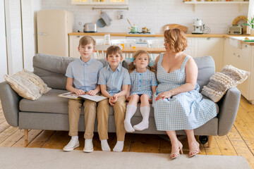 Caring caucasian mother and three young children relaxing at home on sofa and reading interesting book together loving happy caucasian mother and children enjoying storytelling on lazy family weekend.
