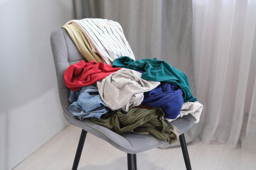 person throws used clothes on the chair. Pile clothes on chair. Heap of used clothes for donation and recycling. Concept of minimalism, mess and wardrobe cleaning