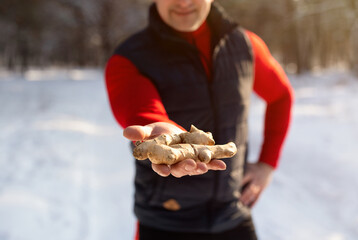 Natural health care concept. Cropped view of senior man in sportswear holding ginger root in winter...