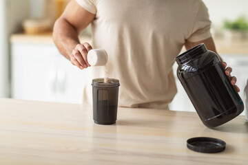 Cropped view of young fit guy making protein shake in kitchen, closeup