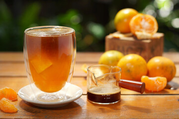 A glass of orange juice served with black coffee decorated with oranges on wood table on nature background.