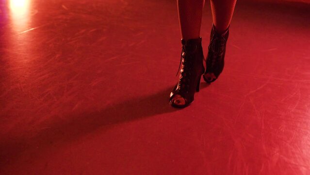 Slender female legs in black shoes. Young woman walking on the floor in high heel shoes in red light