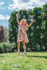 young smiling beautiful girl with long wavy fair hair in sparkling dress jumping, catching soap...