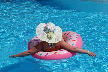 Woman in sun hat and swimsuit swimming on inflatable donut ring in the pool. Beach vacation, relax...