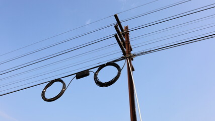 Black boxes and cable reels on poles. Internet box or splitter box with high-speed fiber optic cable hanging on a metal electric pole on a blue background with copy space. Selective focus - obrazy, fototapety, plakaty