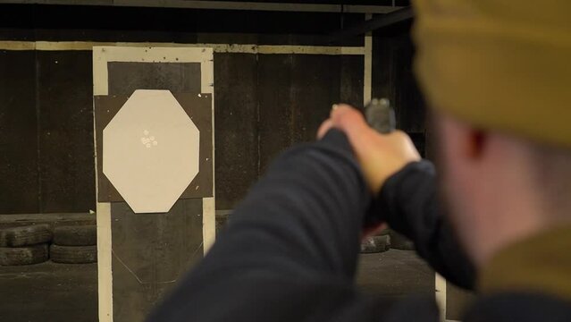 A shooter fires a pistol at a paper target, paper target is in focus, shooter is out of focus, camera moves, soft focus
