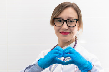 Beautiful young happy doctor woman in medical gloves and glasses with a stethoscope in the hospital shows hand gestures. Selective focus. Portrait. Close-up