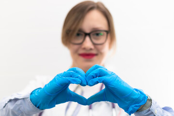 Beautiful young happy doctor woman in medical gloves and glasses with a stethoscope in the hospital shows hand gestures. Selective focus. Portrait. Close-up