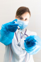 Young woman doctor in a medical mask and gloves with a syringe in her hand and a stethoscope in a...