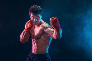 Portrait of muscular kickbox or muay thai fighter who punching in darkness. Sport concept.