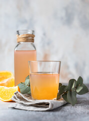 Cold and refreshing fresh orange juice in glass and bottle with fresh orange, grey background.