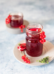 Glass jar with red currant jelly or jam and fresh red currant berries, light background.