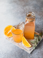 Cold and refreshing fresh orange juice in glass and bottle with fresh orange, grey background.