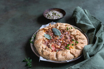 Savory tomato tart, open pie or galette with tomatoes and cheese decorated with aromatic herbs on green background.