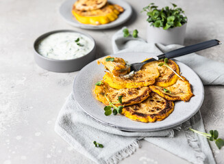 Fried patisson or yellow zucchini with sauce and micro greens, grey background.