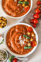 Vegetable soup with baked tomato, bell pepper, cream, breadcrumbs and micro greens in white bowl on concrete background. Top view.