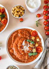 Vegetable soup with baked tomato, bell pepper, cream, breadcrumbs and micro greens in white bowl on concrete background. Top view.