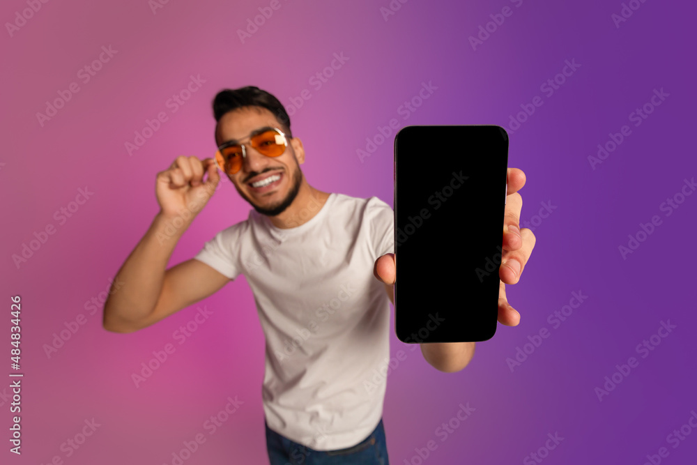 Poster attractive arab man showing smartphone with empty screen in neon light, mockup for ad, mobile app or