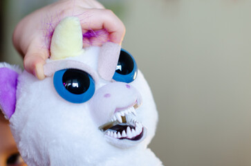 Evil angry aggressive white stuffed toy unicorn held by child’s hand. Background with copyspace
