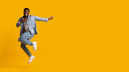 Fototapeta na wymiar Emotional african american millennial man jumping, pointing at copy space