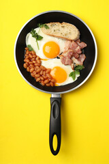 Pan with tasty breakfast on yellow background