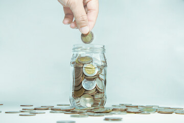 Close-up of a hand taking a coin and dropping it into a glass jar. Savings concept, savings with...