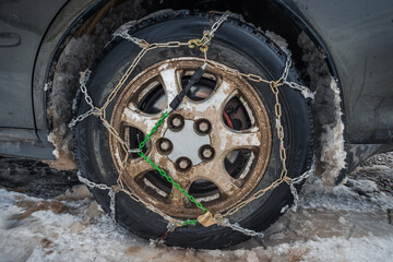 Close-up of snow chains mounted on a snow-covered and dirty car wheel. The concept of safety on snowy roads.