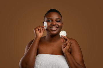 Curvy black woman with acne cleaning skin by cotton pad