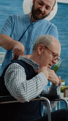 Disabled patient receiving consultation from man nurse in nursing home. Medical specialist using stethoscope for heartbeat checkup and examination with retired person in wheelchair.