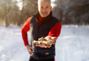 Fit mature man holding ginger root in winter forest, promoting active lifestyle and natural health...