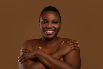 Curvy African American woman with acne embracing herself