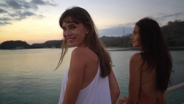 Two lovely brunette models are posing with their backs to the camera with sunset sky in the background in the ocean creek