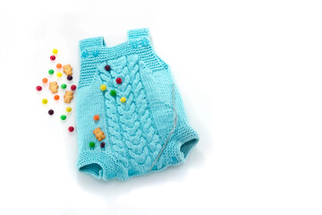 Hand knitted suit for a newborn with an Aran pattern, knitting needles, sweets and bears on a white background. Place for text. Baby blue knitted baby romper in cashmere.