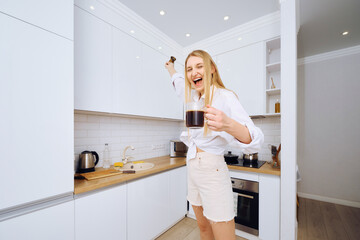 �Cheerful woman dancing and singing with cup of coffee in hand