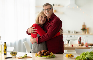 Affectionate senior couple making Christmas dinner together, posing at kitchen near traditional...