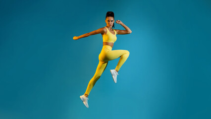 Fototapeta na wymiar Female Jumping Posing In Mid-Air Looking At Camera, Blue Background