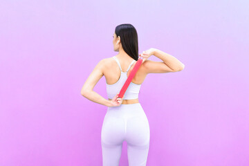 Obraz premium young beautiful woman spending time at home gym, using fitness rubber bands, isolated on plain purple background. Training sport