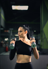 Modern young woman in a sports top with dumbbells in her hands on the background of the gym